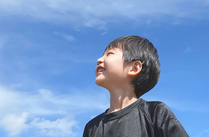 笑顔で歯を見せながら空を見上げてる6歳くらいの男の子
