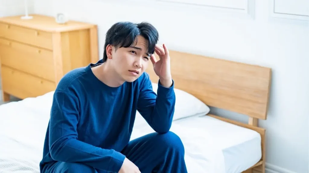 ベットの上でこめかみを抑える男性