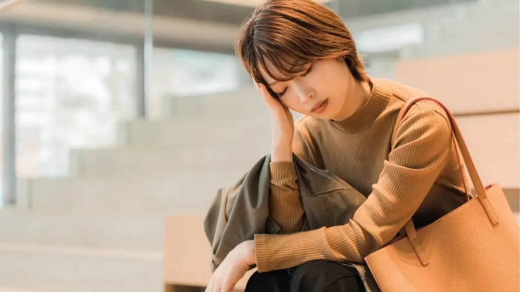 座ってしんどそうに頭を抑える女性