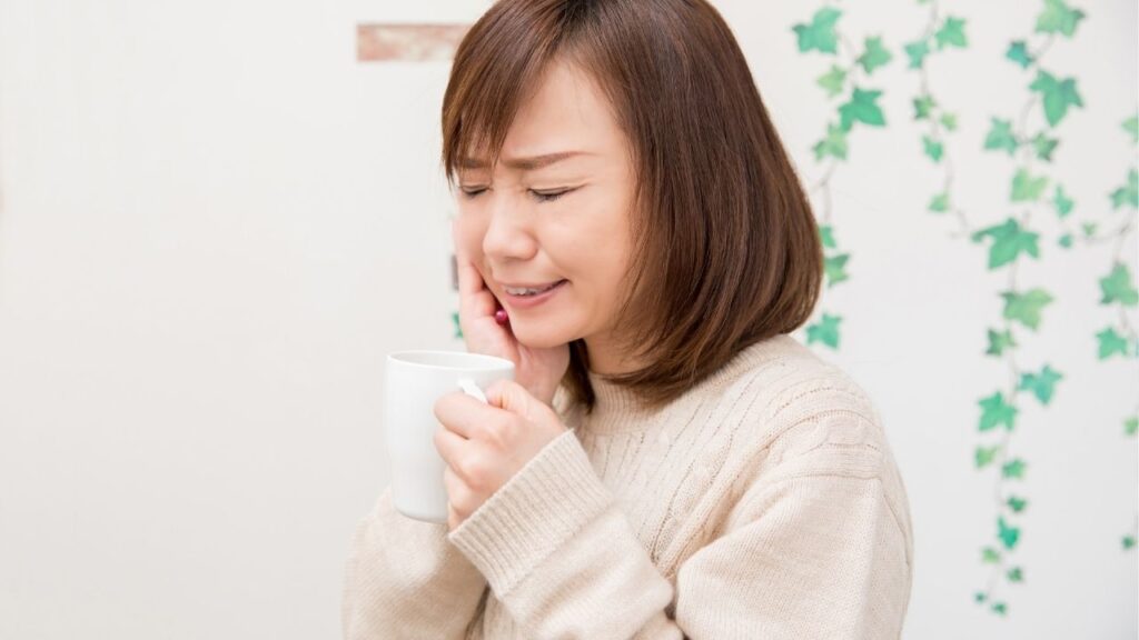 飲み物を飲んで歯を歪める女性