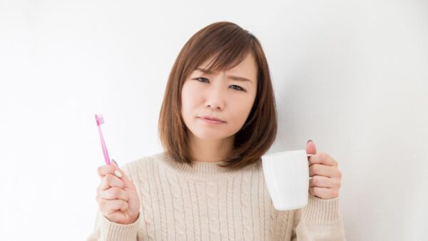 歯ブラシとコップを持ってこまる女性