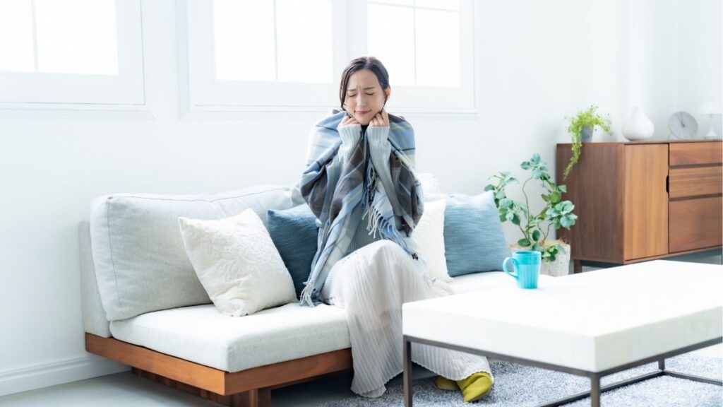 部屋の中で寒そうにストールを羽織っている女性