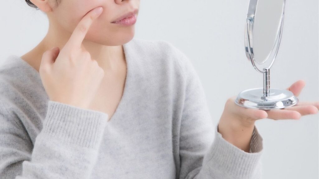 鏡を持って鼻と歯の間を指で抑える女性