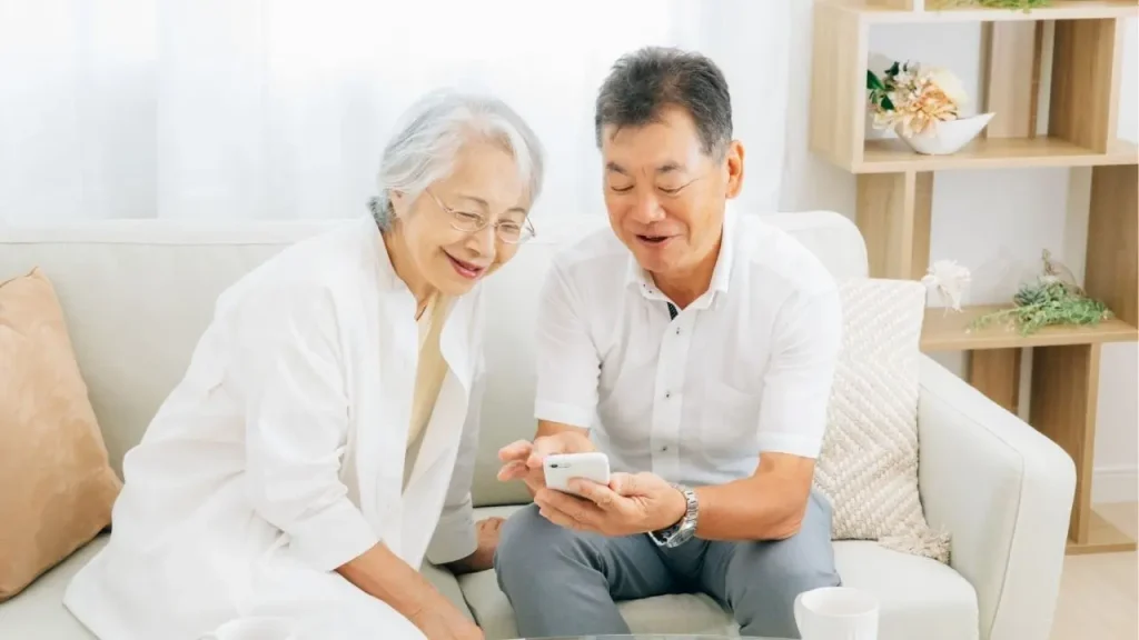 ソファーに座って笑顔で電話を見ている老夫婦